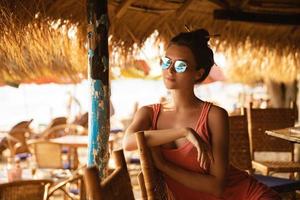 mujer joven con gafas de sol sentada en el bar de la playa foto