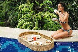 Young happy woman with a floating breakfast in the pool photo