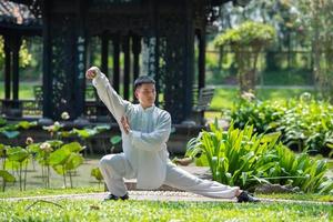 entrenamiento de hombre asiático con tai chi en la mañana en el parque, artes marciales chinas, atención saludable para el concepto de vida saludable. foto