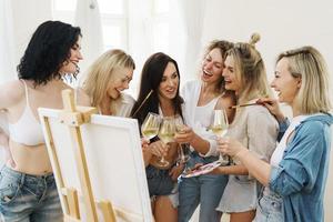 Group of women paint on canvas and drinking white wine during party at home photo