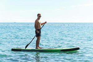 Young male surfer riding standup paddleboard in ocean. photo