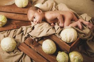 Little baby is lying in the box with a lot of cabbages around photo