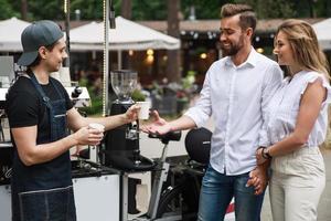 Barista man selling coffee to young couple in the movable coffee shop photo