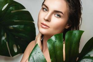 Young woman with a smooth skin holding Monstera deliciosa plant leaf photo
