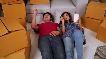 Slow motion shot, Young couple lying at front of sofa on floor and checking boxs after relocation in their new home, new house concept video