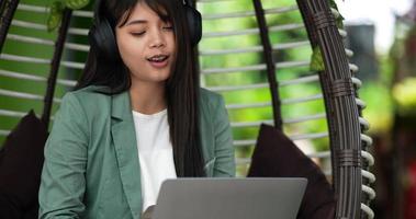 Close up shot, Pretty young Asian woman sitting and enjoy to listening musice from wireless headphone and singing together while working on laptop at cafe. Business, relaxing and lifestyle concept.