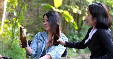 Group beautiful Asian women friends travelers relaxing in camp chairs at tent, They are cheering and drinking beer during camping, talking with fun and happy together video