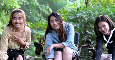 Handheld-Nahaufnahme, Gruppe junger asiatischer Frauen, die auf ihren Stühlen sitzen und es genießen, Wasser im Bach zu spritzen, während sie im Naturpark campen, sie reden und lachen Spaß zusammen. video