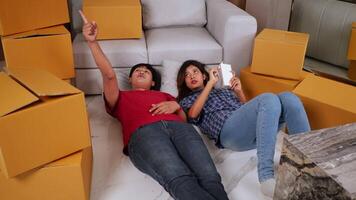 Slow motion shot, Young couple lying at front of sofa on floor and checking boxs after relocation in their new home, new house concept video