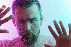 Handsome young man captured through wet glass in colorful neon light photo