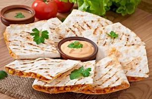 Mexican Quesadilla sliced with vegetables and sauces on the table photo