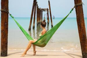 Woman is relaxing in the hammock hanging on old beams from the broken pier photo