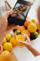 mano femenina con un smartphone tomando fotos de vidrio con jugo de naranja
