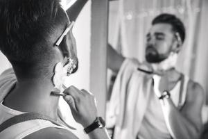 Man looking in the mirror and shaving his beard with a straight razor photo