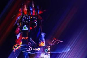 Model in image of Native american with neon makeup, which made of fluorescent paint in ultraviolet light. photo