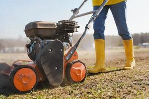 Woman villager is using aerator machine to scarification and aeration of lawn or meadow photo