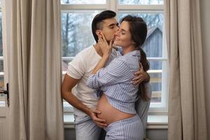 joven pareja embarazada sensual en abrazo al lado de la ventana. foto