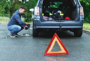 Warning triangle and man changing car wheel photo