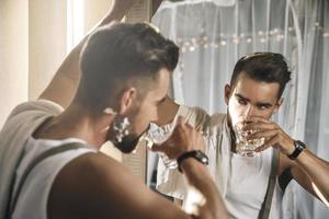 un hombre guapo con un vaso de whisky se mira en el espejo foto