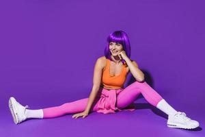 Cheerful woman wearing colorful sportswear sitting against purple background photo