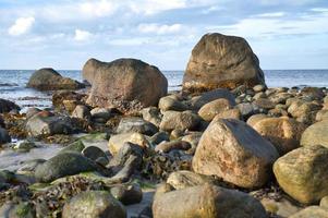 Big stones on stone beach in front of sea with clouds in sky. Denmark in Scandinavia photo