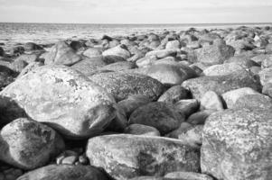 Big stones on stone beach in black and white taken in front of sea with clouds in sky photo