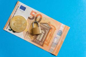 Shiny golden bitcoin and small brass padlock on a fifty euro banknote. photo