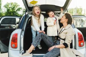 Young mother and her adorable dauthers sitting in a car trunk. photo