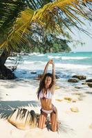joven mujer sexy lleva bikini posando a la sombra de una palmera