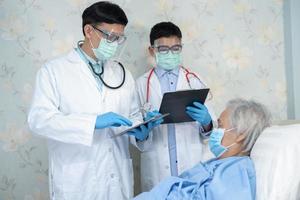 Asian doctor team check old senior lady patient for disease to motivation new normal to treat infection Covid19 Coronavirus at hospital ward. photo