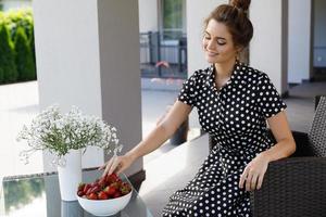 hermosa mujer con un hermoso vestido con un patrón de lunares sentado en un patio y comiendo fresa foto