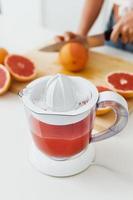 exprimidor de cítricos lleno de jugo de pomelo fresco en la mesa de la cocina blanca foto