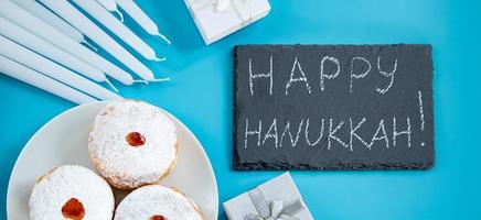 Happy Hanukkah. Jewish dessert sufganiyot donuts on blue background. Symbol of religious Judaism holiday. Inscription on chalk board.
