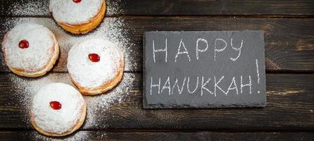 Happy Hanukkah. Traditional dessert Sufganiyot on dark wooden background. Donuts, candles and gifts. Celebrating Jewish holiday. photo