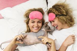 dos hermosas chicas acostadas en una cama con un gato foto