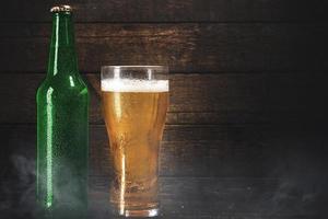 botella verde y vaso de cerveza lager pálida sobre fondo de madera foto