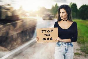 mujer activista con pancarta detener la guerra cerca de la carretera con tanques en movimiento foto