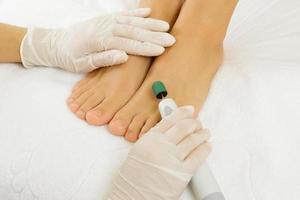 Pedicure master work. Closeup of female feet and hands in gloves with a special machine tool. photo