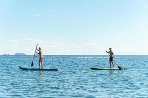 surfistas masculinos y femeninos montando paddleboards de pie en el océano. foto