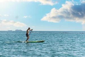 Young male surfer riding standup paddleboard in ocean. photo