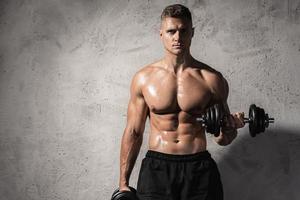 Young and muscular bodybuilder man working out with dumbbells photo