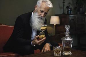 Handsome and bearded senior man drinking whiskey photo