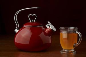 una tetera roja sobre un fondo oscuro con una taza de té foto