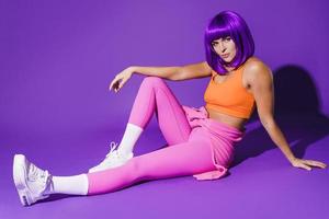 Young woman wearing colorful sportswear sitting against purple background photo