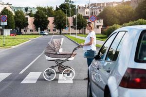 Young mother with the baby pram is walking by the crosswalk photo