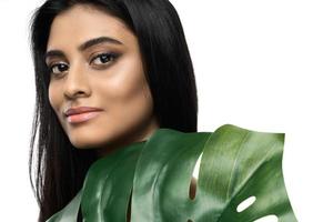 hermosa mujer india con una piel suave sosteniendo una hoja tropical verde foto