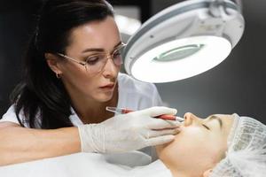 Permanent makeup artist and her client during lip blushing procedure photo