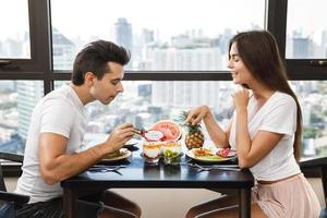 pareja feliz comiendo un desayuno saludable en un apartamento moderno con grandes ventanales y vistas a la ciudad foto