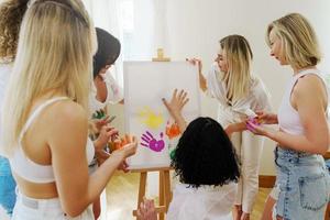 Group of women paint on canvas and drinking white wine during party at home photo