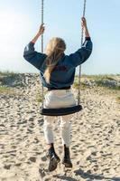 foto trasera de una mujer joven columpiándose en un columpio en la playa.